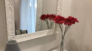 A bathroom vanity with a white countertop, a mirror with a textured frame, and a vase with red flowers. - B&B Geolja (Gioia Tauro)