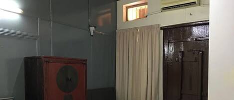 Una habitación pequeña y tenuemente iluminada, con una cama individual, un armario de madera y una ventana con cortinas.