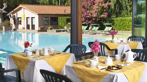 A poolside dining area with tables set for breakfast, overlooking a swimming pool and a building with a tiled roof. - Hotel Villalago (Magione)