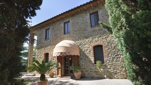 A stone building with a large umbrella canopy, potted plants, and a paved entrance. - Hotel Villalago (Magione)