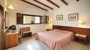 A bedroom with a large bed, wooden headboard, a desk with a television, a chair, a window with curtains, and two wall-mounted lamps. - Hotel Villalago (Magione)