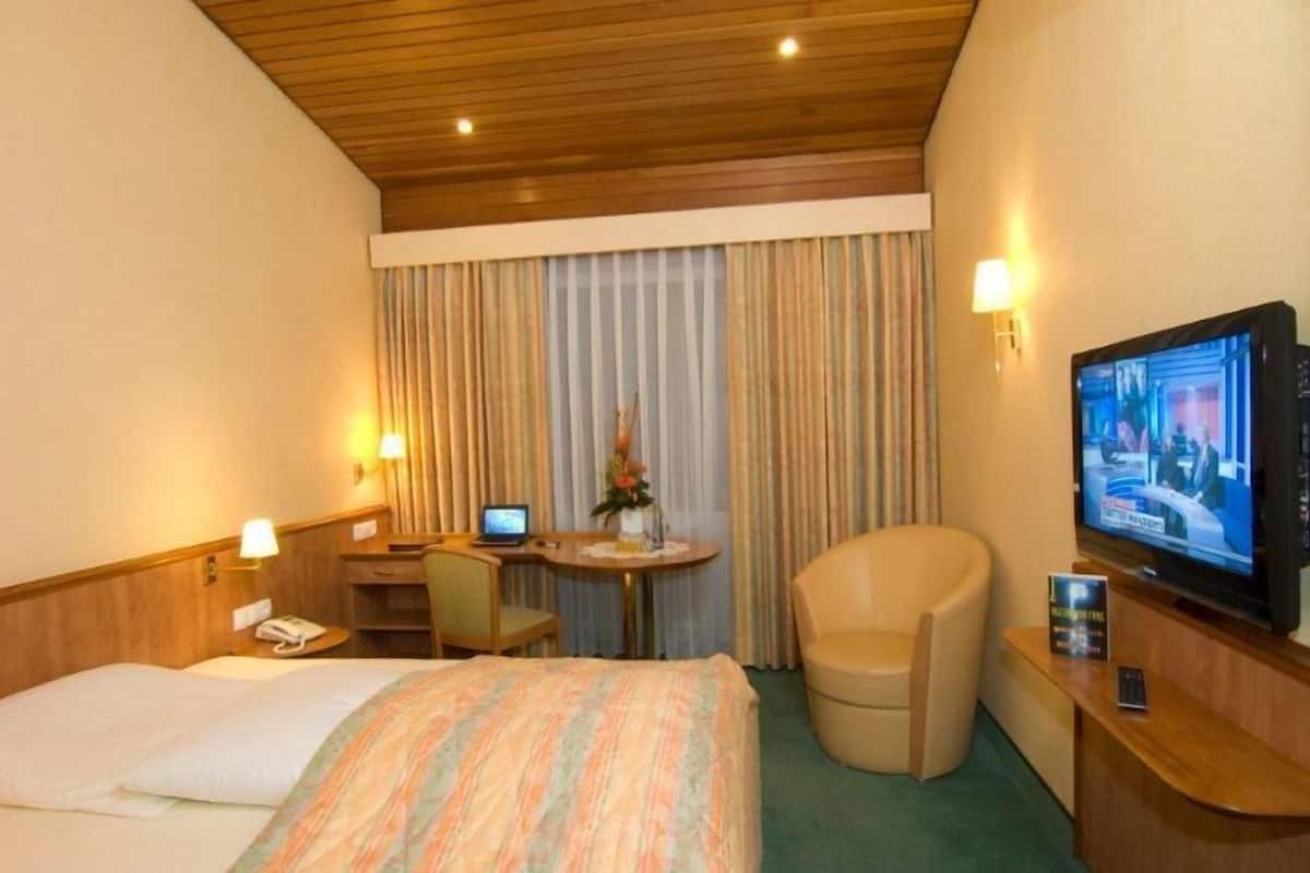 A hotel room with a bed, desk, chair, TV, and curtains.