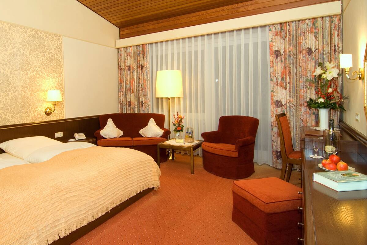 A hotel room with a large bed, a sofa, a desk with a lamp, and a chair.