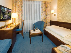 A hotel room with a bed, a desk with a chair, a television, a table with a bottle of wine and a glass, and a telephone. - Burghotel (Geislingen an der Steige)