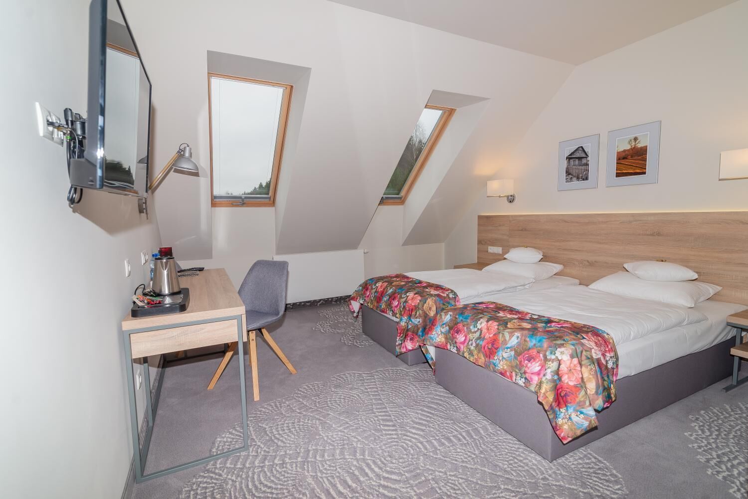 Una habitación de hotel moderna con escritorio, dos camas, tragaluces y obras de arte en las paredes.