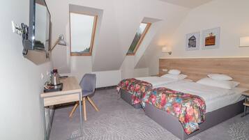 A modern hotel room with a desk, two beds, a skylight, and artwork on the walls.