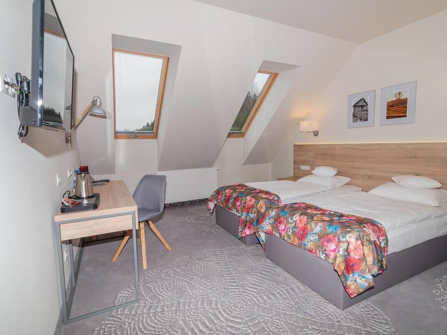A modern hotel room with a desk, two beds, a skylight, and artwork on the walls.
