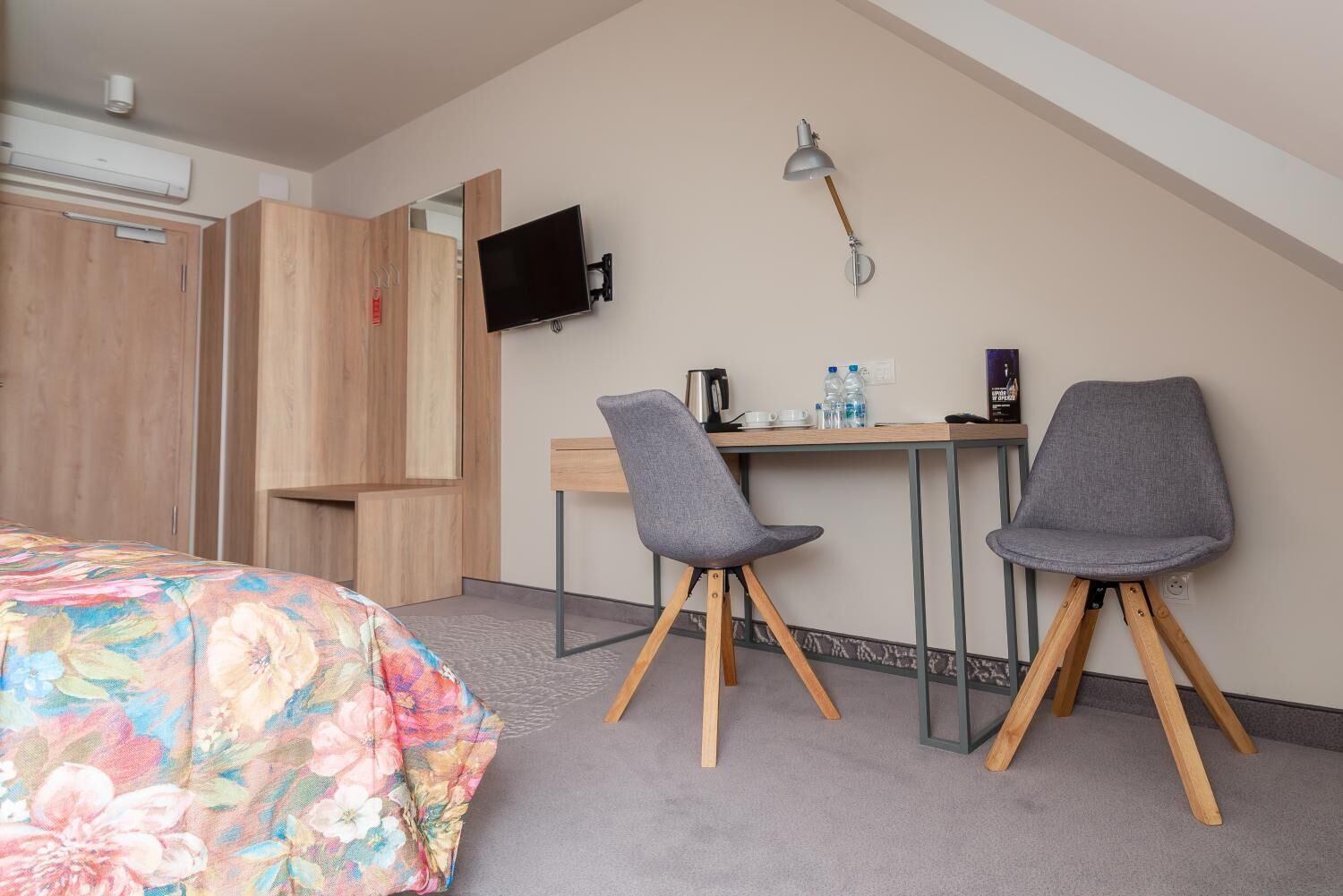 Una habitación de hotel con una cama, un escritorio, dos sillas, un televisor y una lámpara.