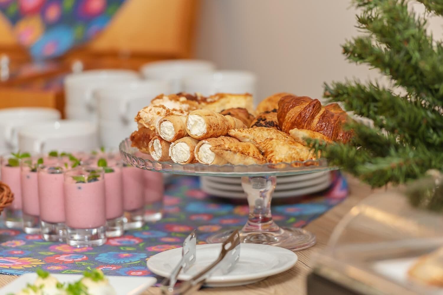 Ein Frühstücksbuffet mit Gebäck, Brötchen und rosa Getränken auf einer blumigen Tischdecke.