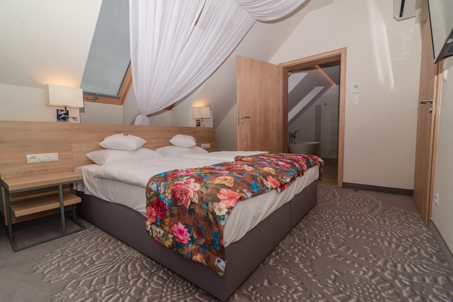 A bedroom with a bed, bedside tables, a desk, a mirror, and a door leading to a bathroom.