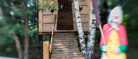 A wooden staircase leading to a treehouse with a small door and windows.