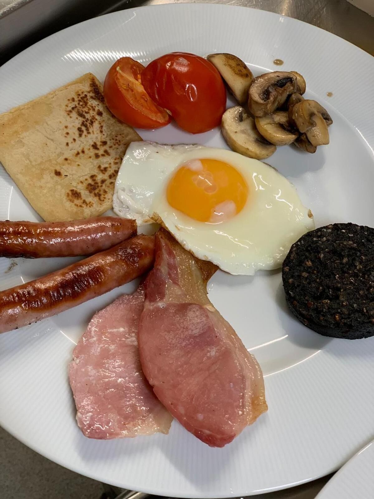 A plate with a fried egg, sausages, bacon, ham, mushrooms, and tomatoes.