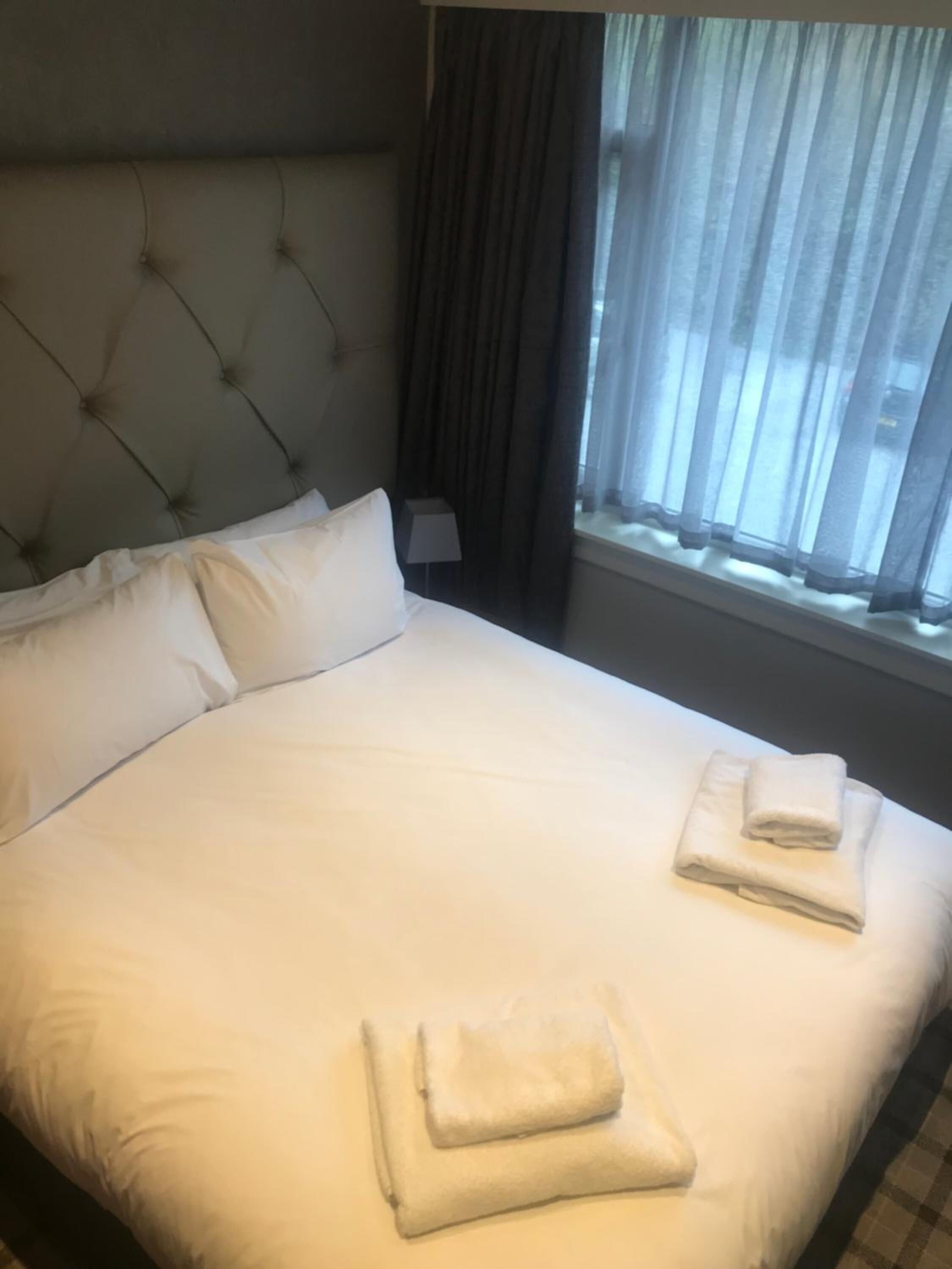 A neatly made bed with white linens and two folded towels on the bed.