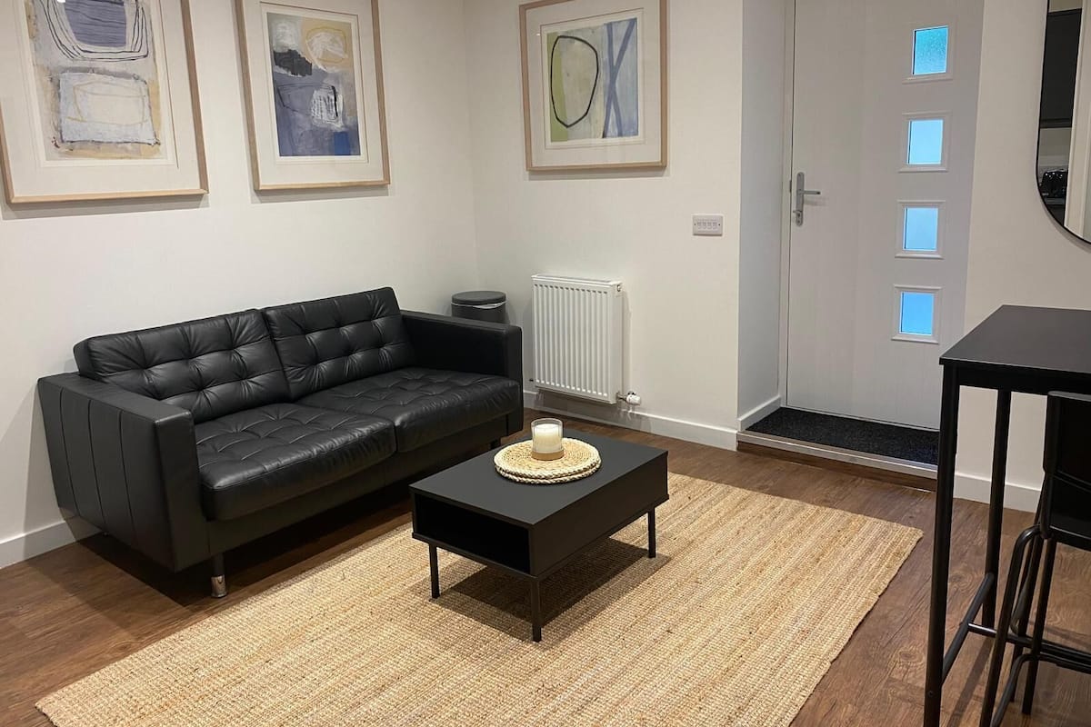 A modern living room with a black leather sofa, a coffee table, and framed abstract art on the walls.