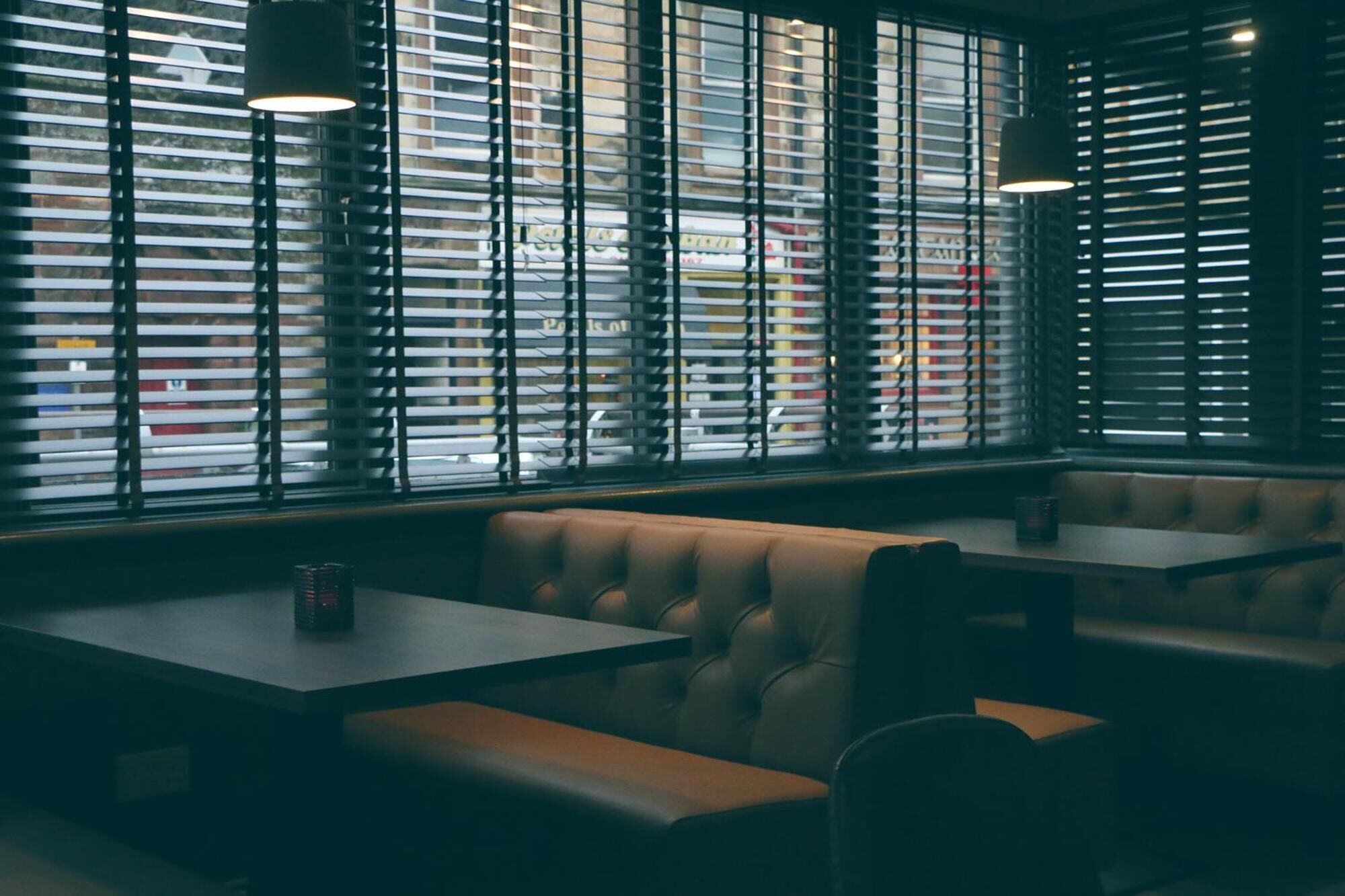 A restaurant interior with booths, tables, and large windows with blinds.
