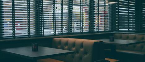 A restaurant interior with booths, tables, and large windows with blinds.