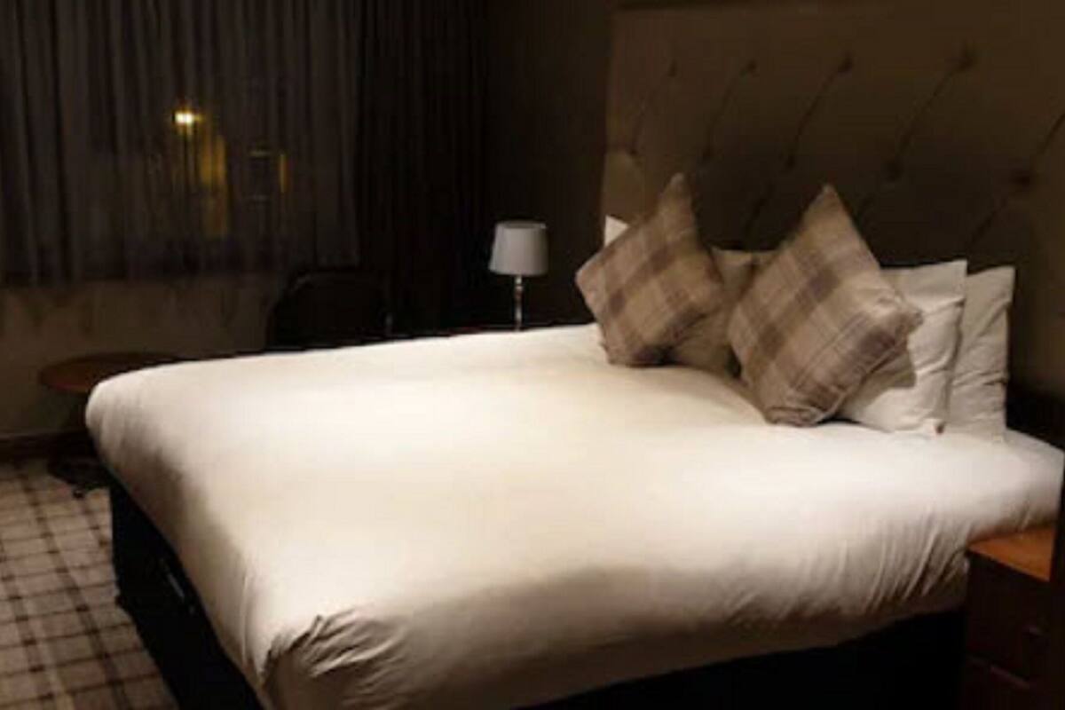 A hotel room with a large bed, a nightstand, a lamp, and a window with curtains.