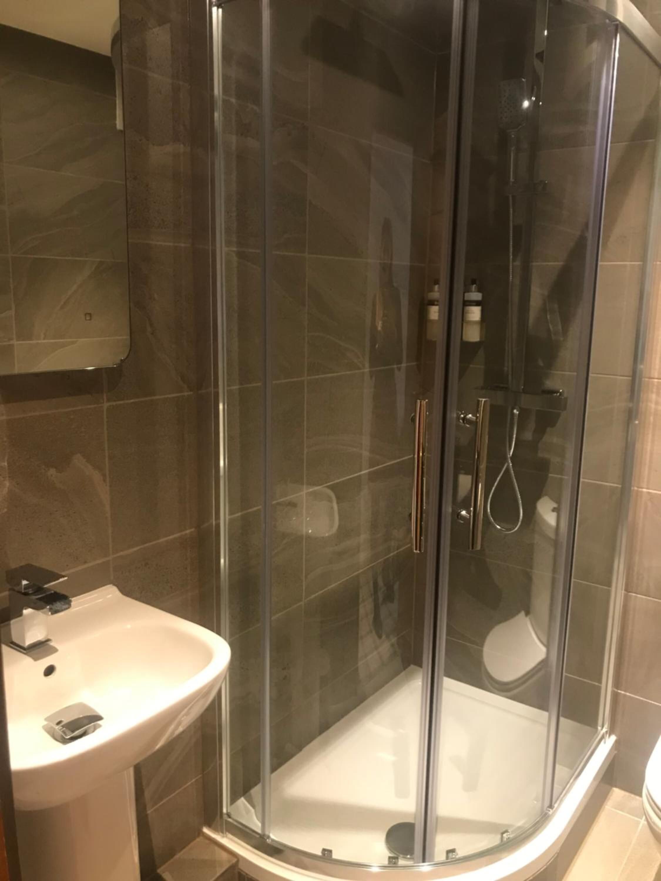 Ein modernes Badezimmer mit einer Duschkabine, einem weißen Waschbecken und einem Spiegel darüber.