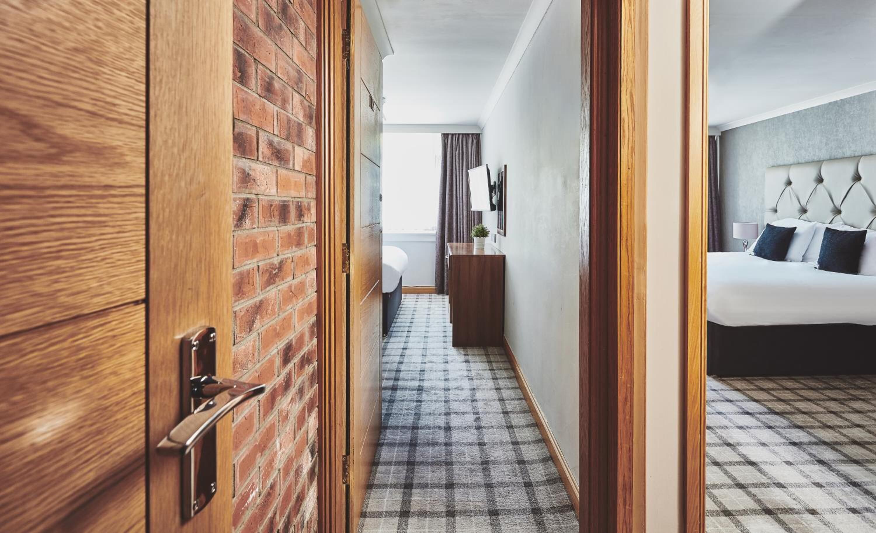 A hotel room with a checkered floor, a bed with a tufted headboard, a bedside table, and a mirror on the wall.