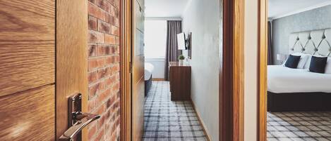 A hotel room with a checkered floor, a bed with a tufted headboard, a bedside table, and a mirror on the wall.