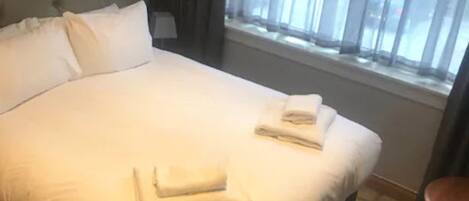 A neatly made bed with folded towels and a window with curtains.