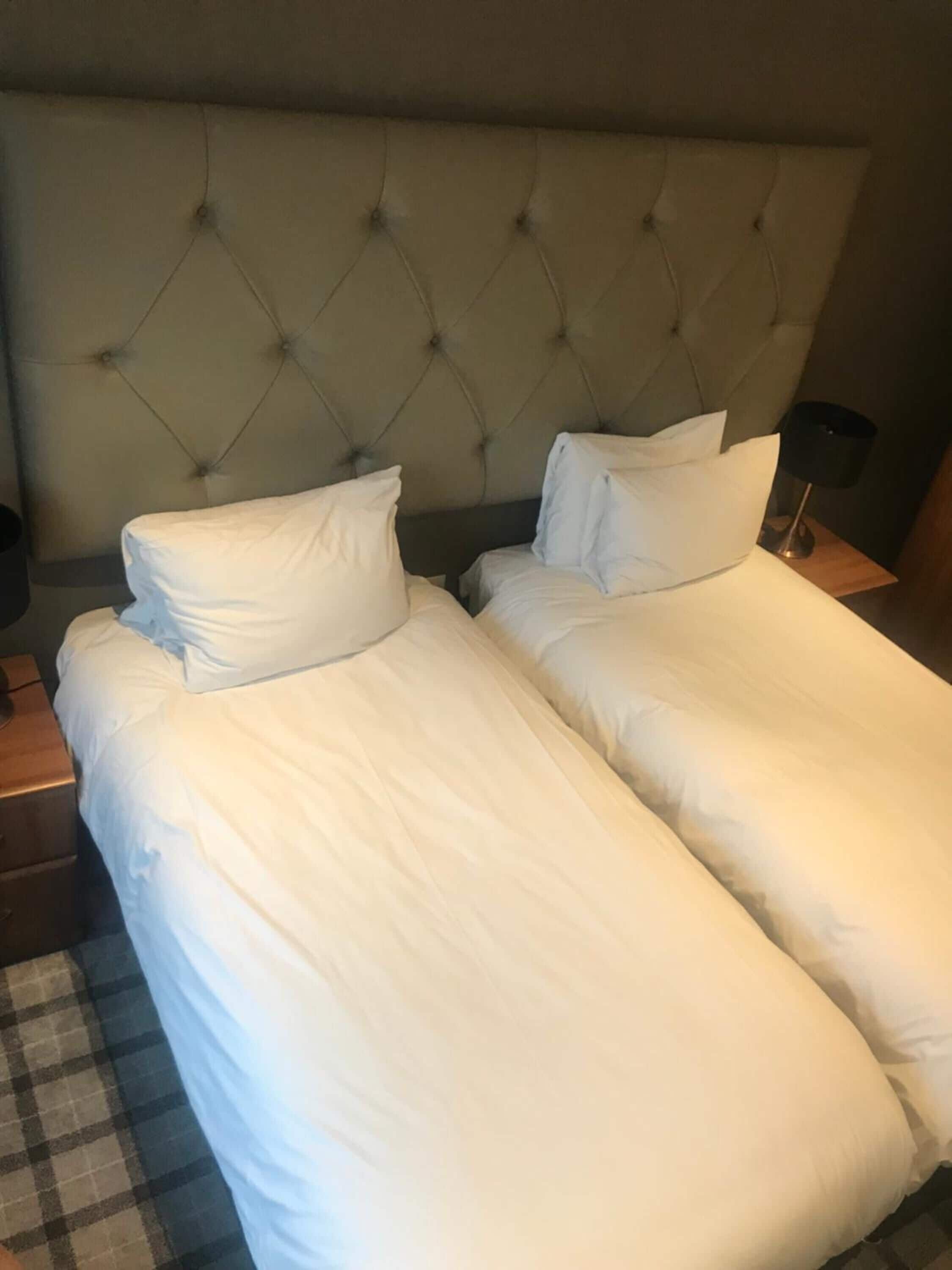 A hotel room with two single beds, a tufted headboard, a checkered floor, and a nightstand with a lamp.