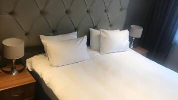Una cama bien hecha con un cabecero capitonado, una lámpara de noche y un suelo a cuadros.