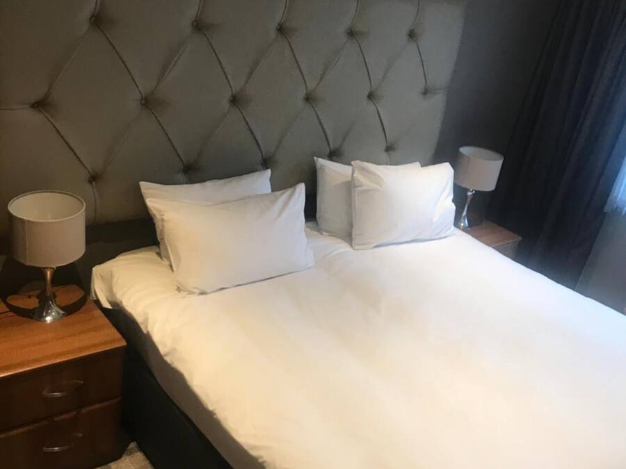 A neatly made bed with a tufted headboard, a bedside lamp, and a checkered floor.