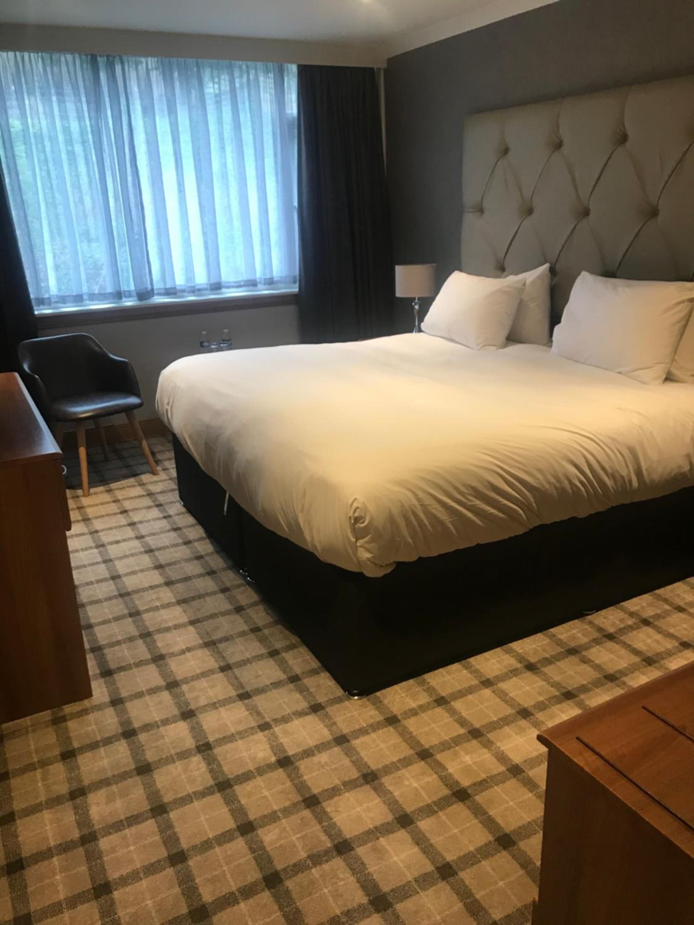A hotel room with a large bed, a chair, a desk, and a window with curtains.