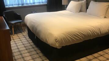 A hotel room with a large bed, a chair, a desk, and a window with curtains.