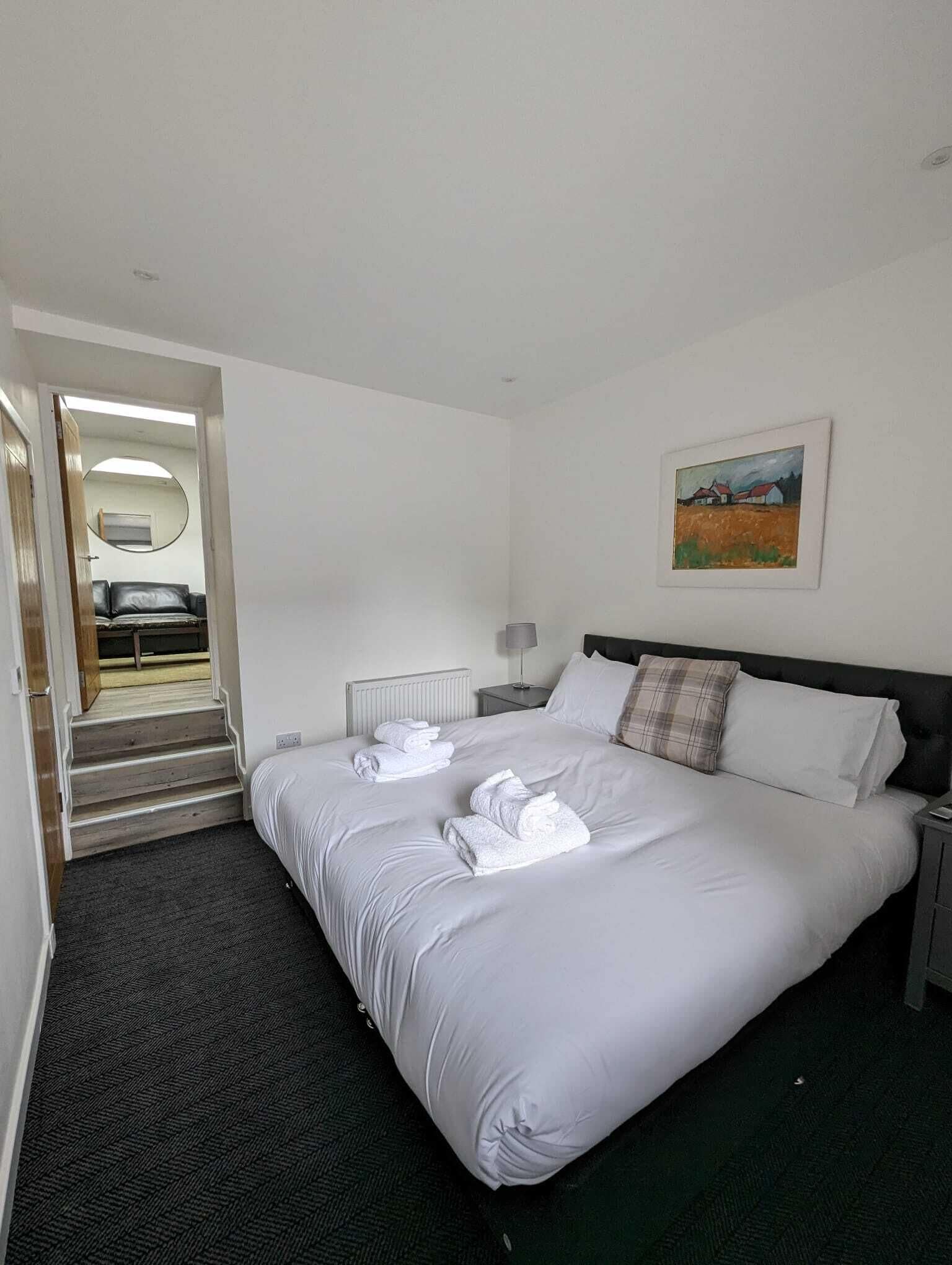 A hotel room with a large bed, a painting on the wall, and a view of the outside through an open door.