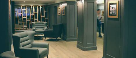 A modern lounge area with grey upholstered armchairs, a round coffee table, and a wooden floor.