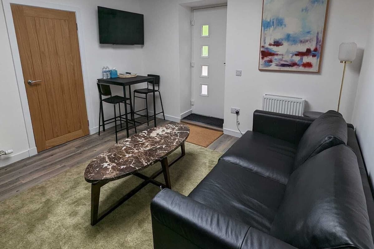 A modern living room with a black leather sofa, a marble coffee table, a wooden door, a television, and a skylight.