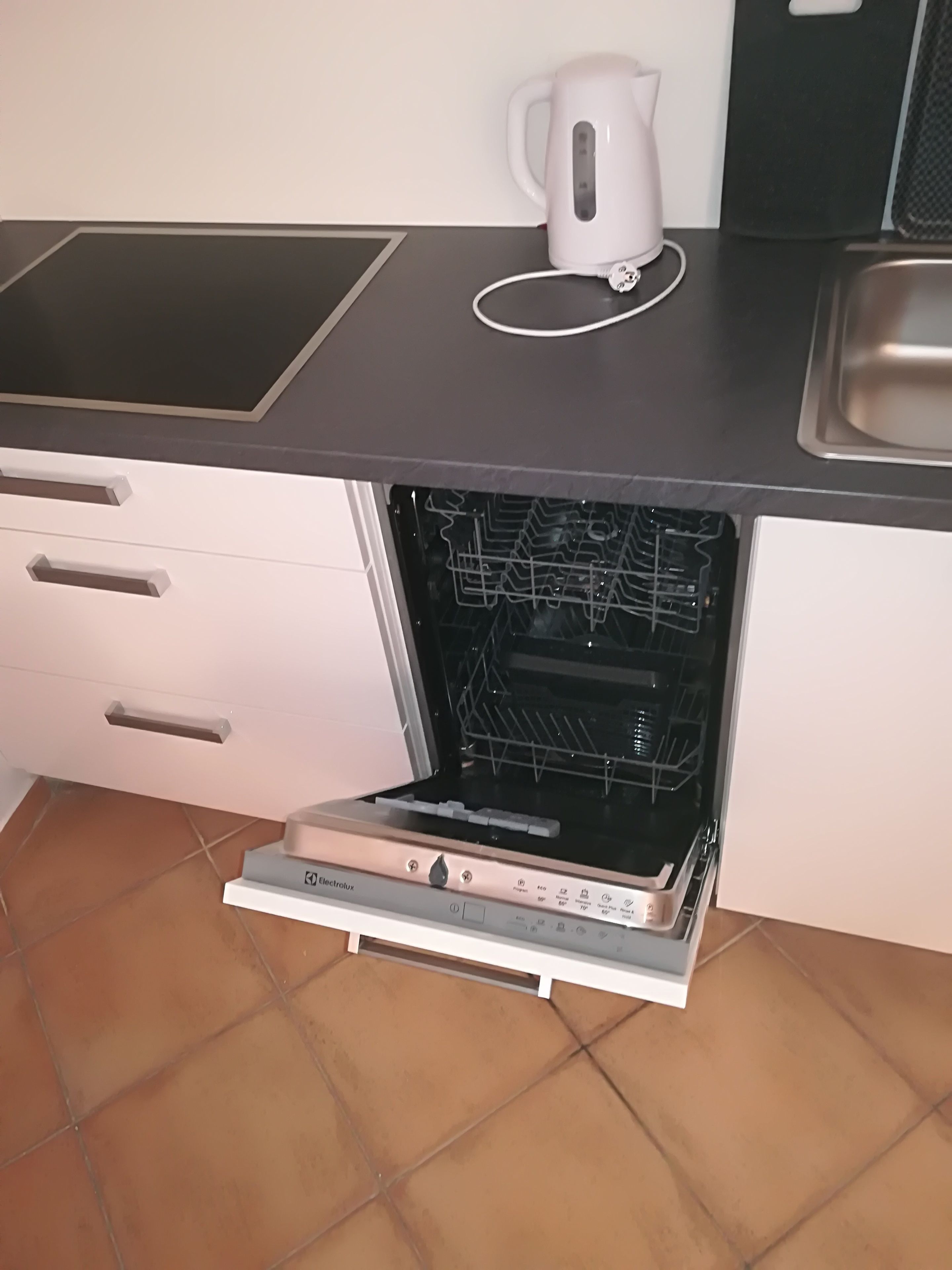 A kitchen with a built-in oven, a kettle, and a sink.