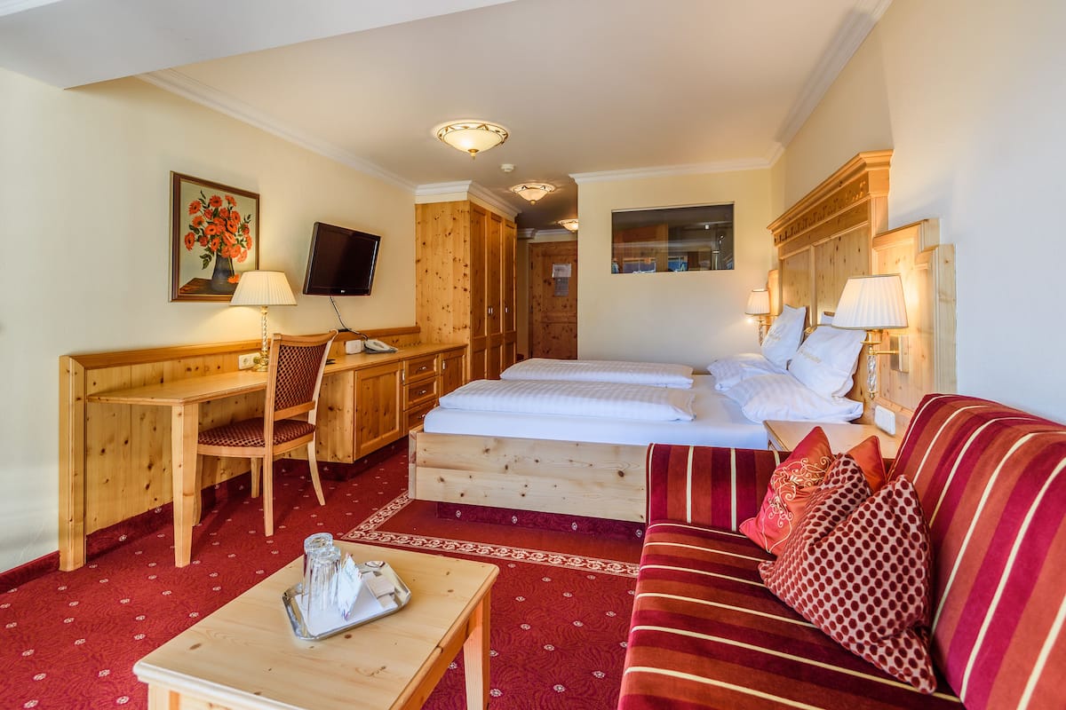 Ein Hotelzimmer mit einem Holztisch, einem Bett mit weißer Bettwäsche, einem roten Sofa mit Streifen und einem an der Wand befestigten Fernseher.