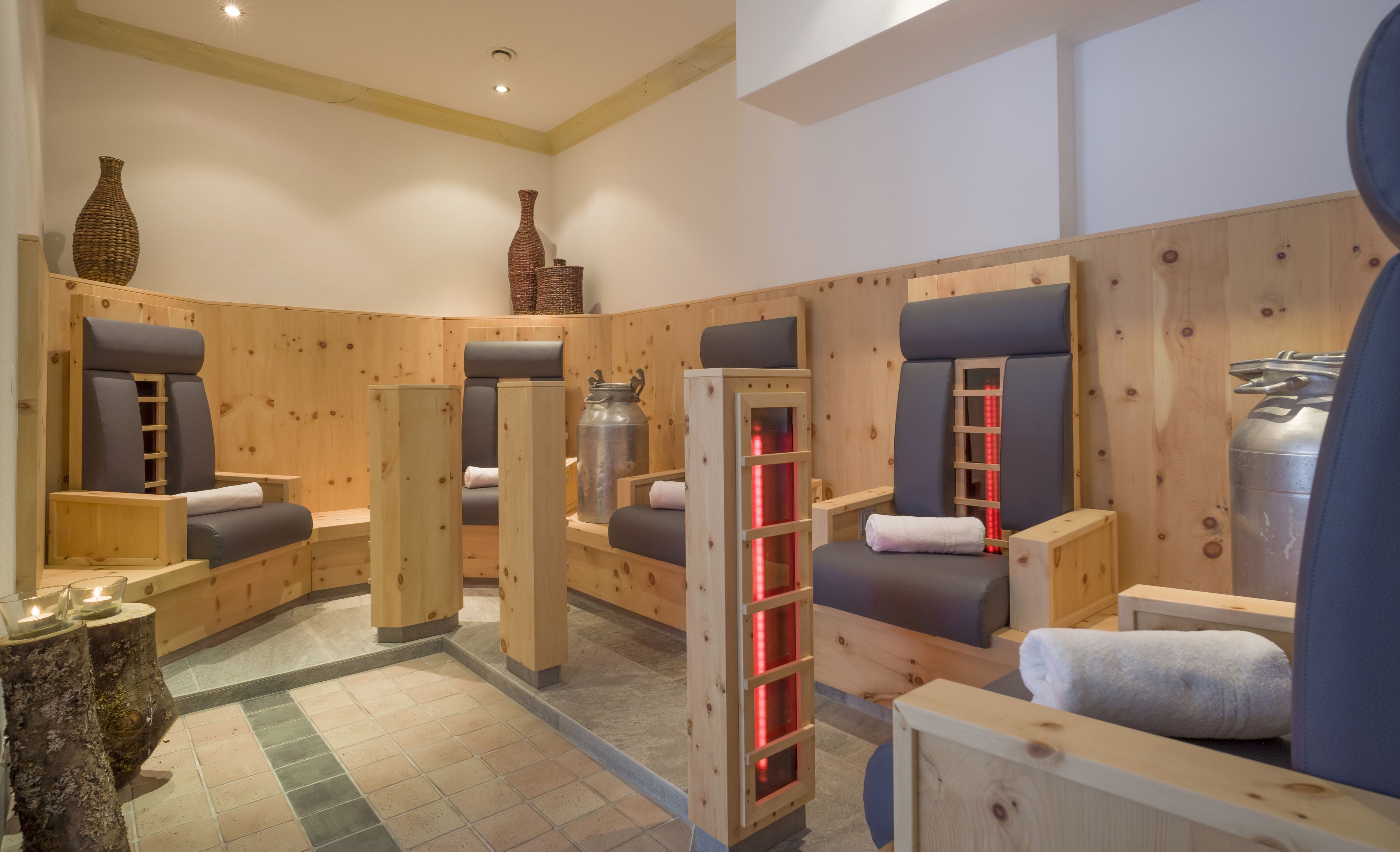 Une salle de sauna avec des bancs en bois, un grand récipient en métal et une étagère éclairée en rouge.