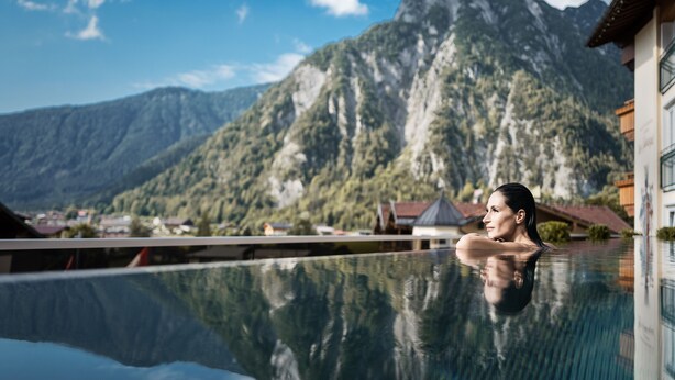 Eine Person entspannt sich in einem Pool vor einer Bergkulisse.