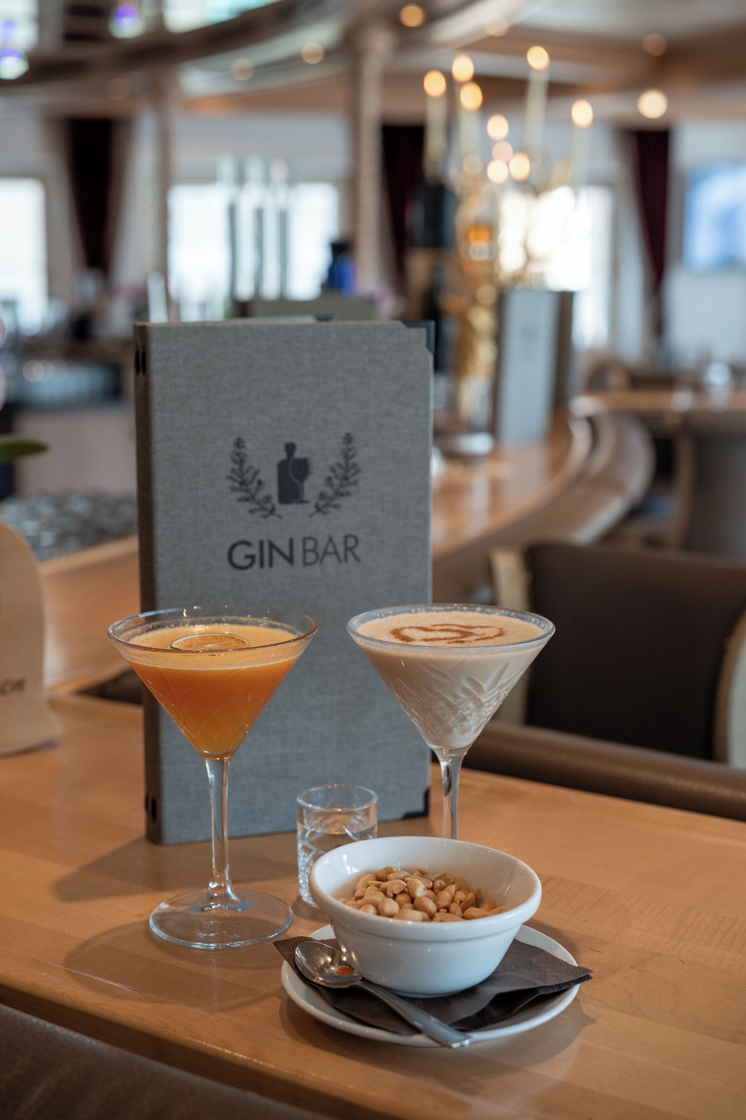A bar area with two martini glasses and a bowl of nuts on a wooden table.