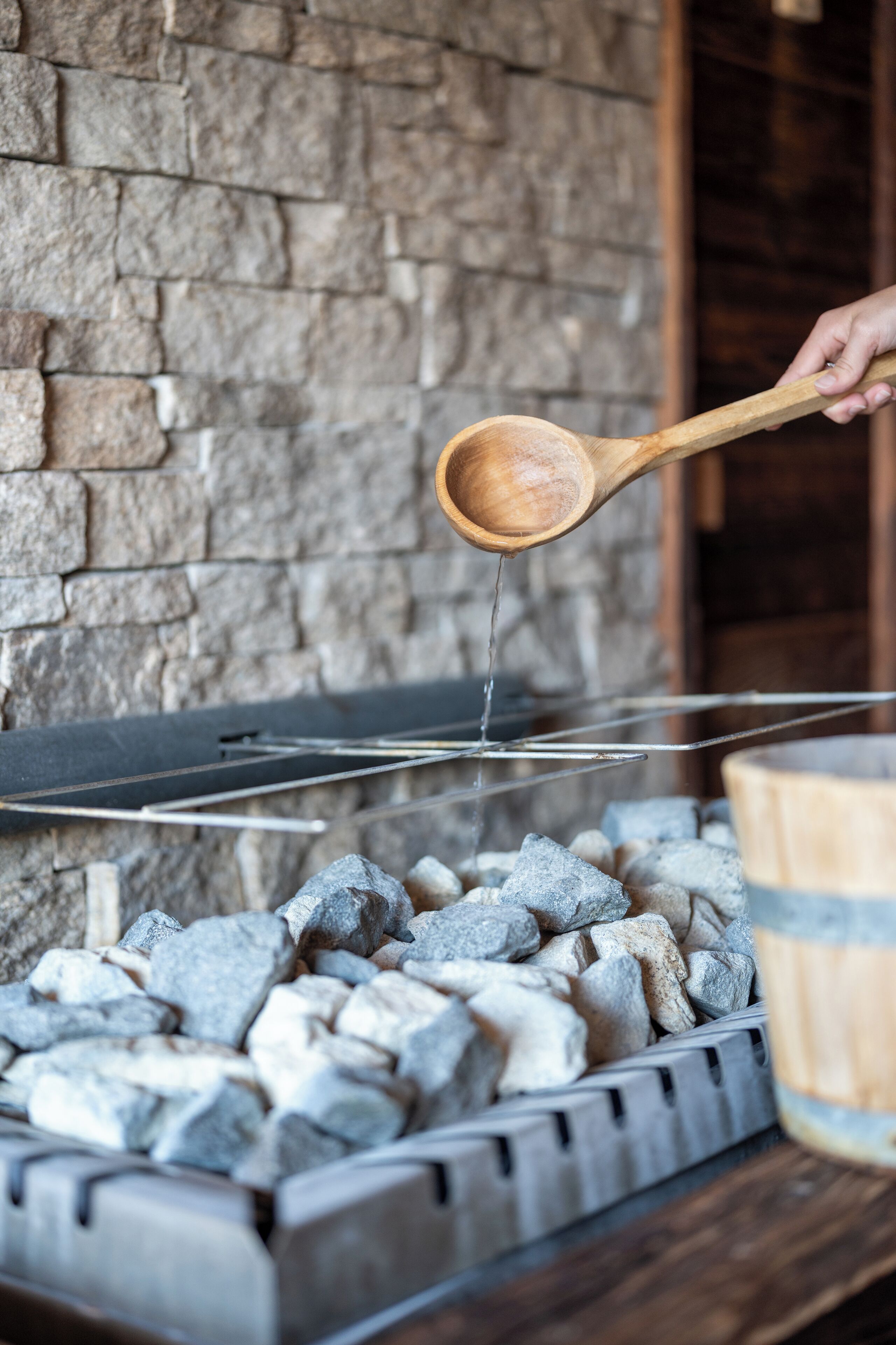 A hand pouring water from a wooden ladle over charcoal in a grill.