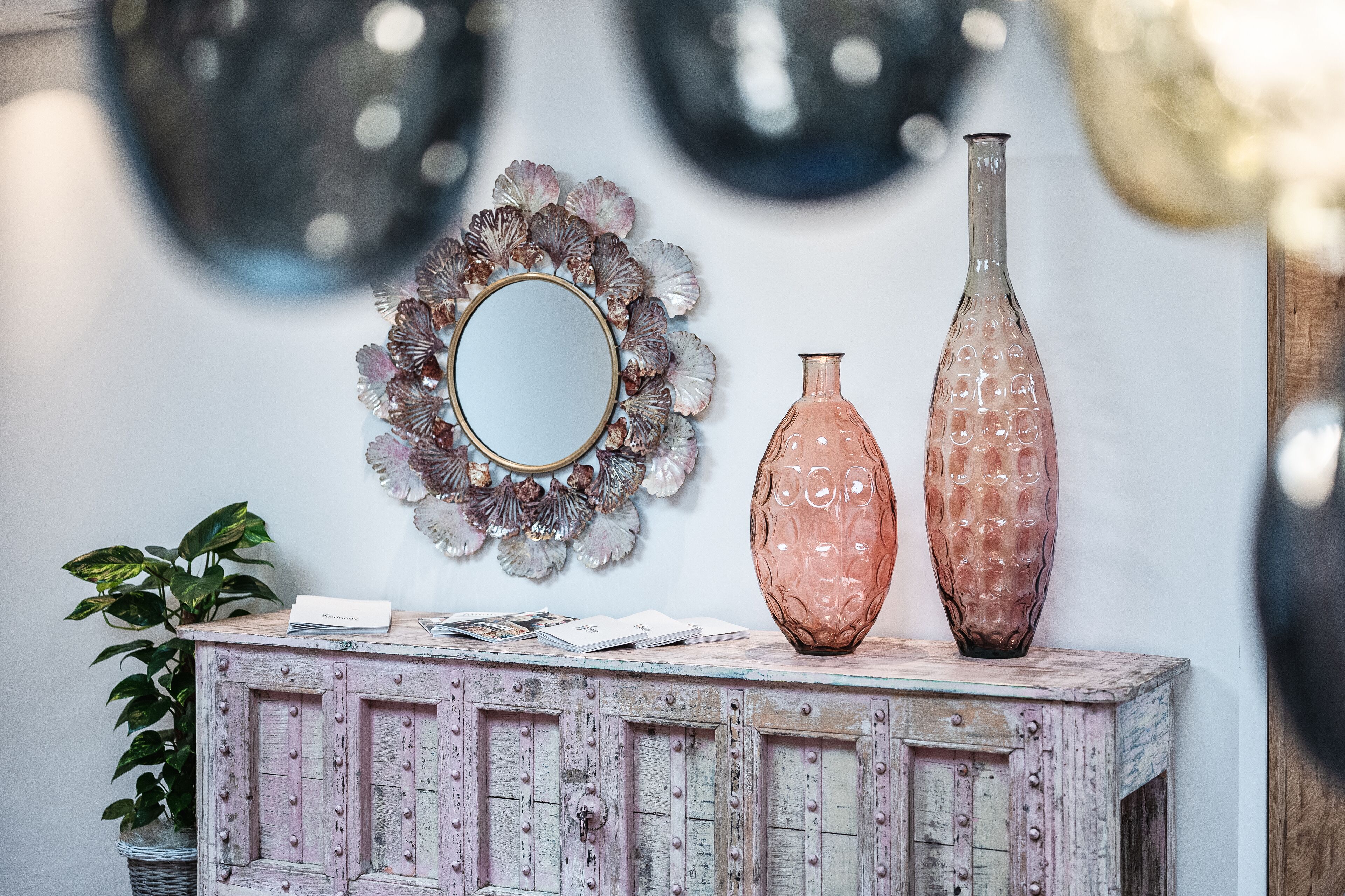 A vintage wooden cabinet with decorative items including a mirror, two vases, and a wall-mounted shell decoration.