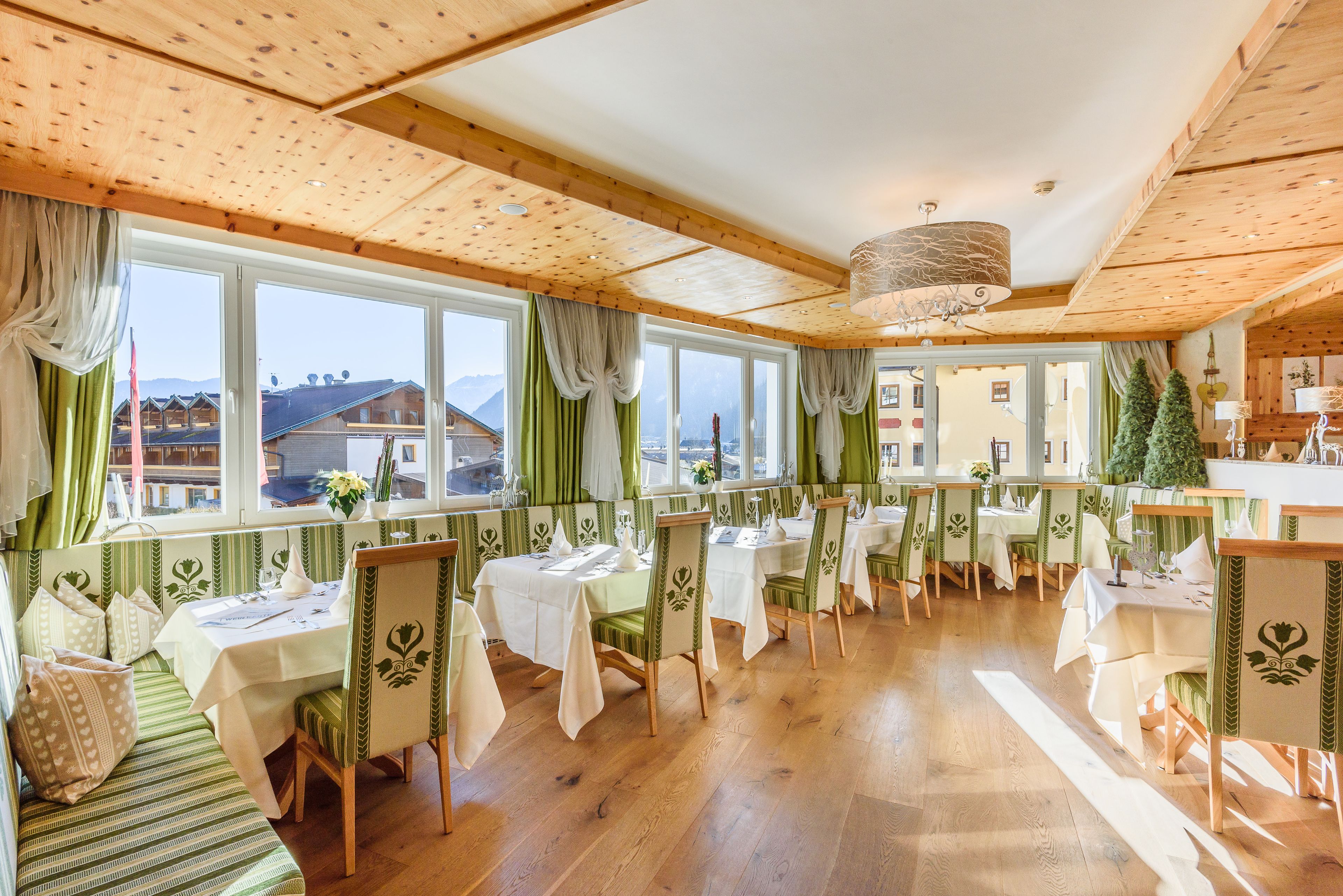 Comedor con vigas de madera en el techo, ventanas amplias con cortinas y mesas dispuestas para comer.