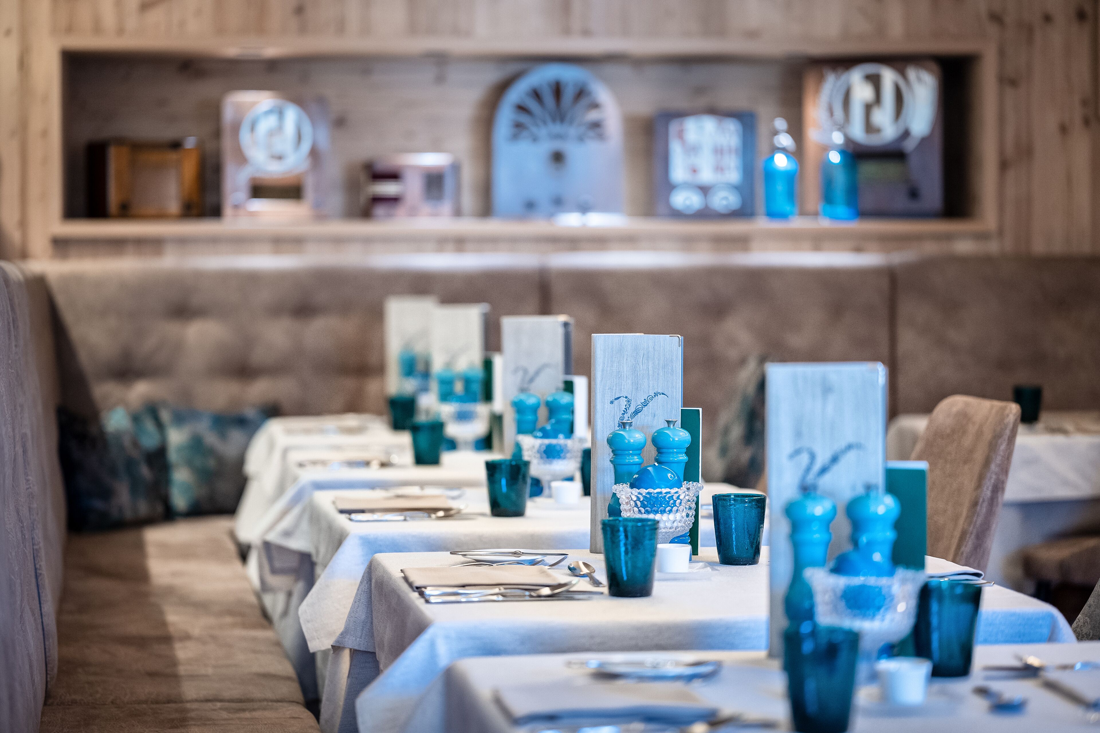 Un espace repas avec des tables dressées pour le service, agrémenté de verres bleus et de nappes blanches.