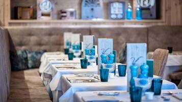 Un espace repas avec des tables dressées pour le service, agrémenté de verres bleus et de nappes blanches.