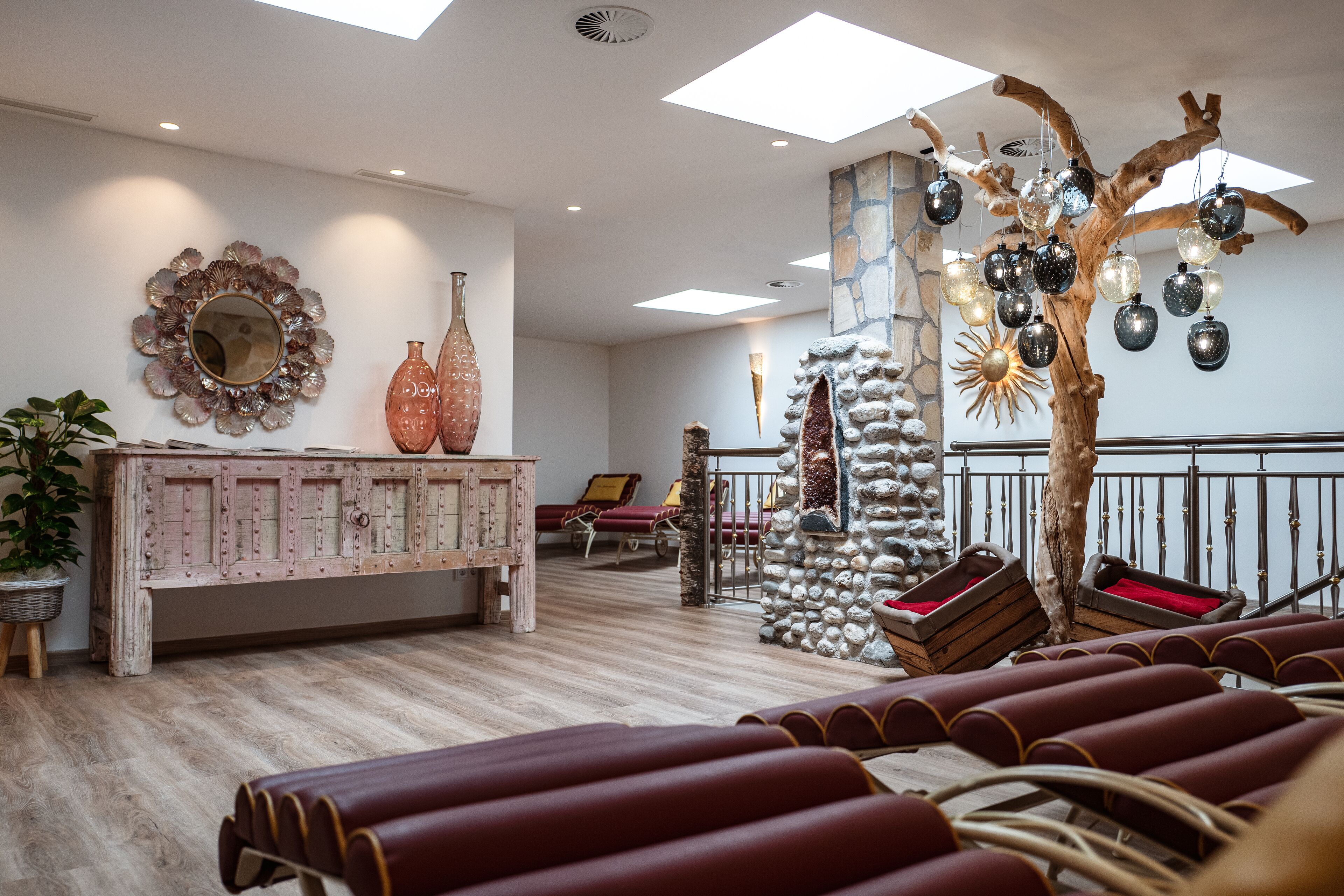 A spacious room with a wooden bench, a decorative tree with hanging ornaments, and a stone pillar.