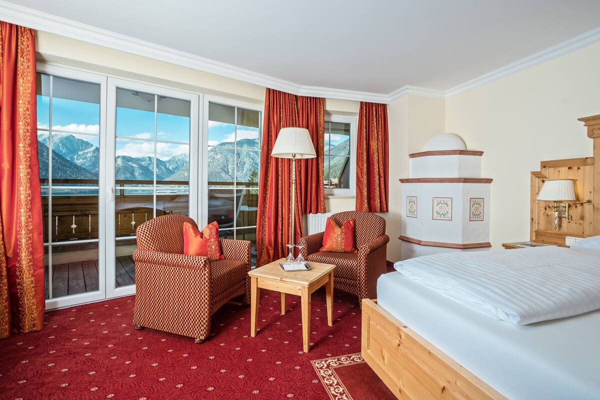 Ein Hotelzimmer mit einem Bett, zwei Sesseln, einem kleinen Tisch und Bergblick durch große Fenster.
