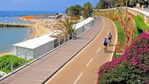 A coastal walkway with a paved path, a beach, and a clear blue sky. - Casa Parini (Imperia)