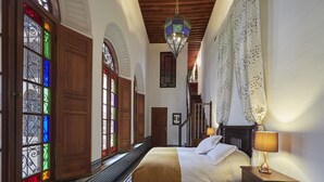 Un dormitorio con cama, mesita de noche, lámpara, alfombra estampada y vista de una escalera.