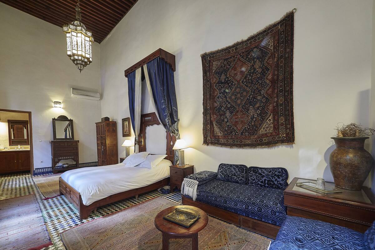 A traditional room with a bed, a sofa, a small table, and a large tapestry.