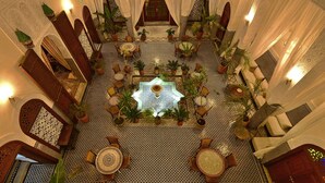 Un patio interior con una fuente central, rodeado de zonas de estar y plantas en macetas.