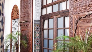 Un patio tradicional marroquí con puertas de madera ornamentadas, suelo de baldosas y plantas en macetas.
